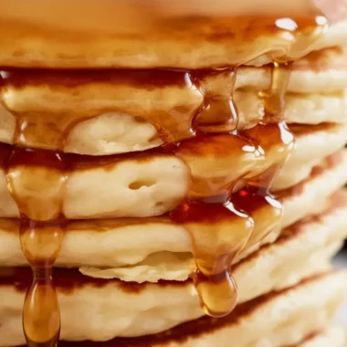 Stack of fluffy pancakes served with syrup and berries on a plate.