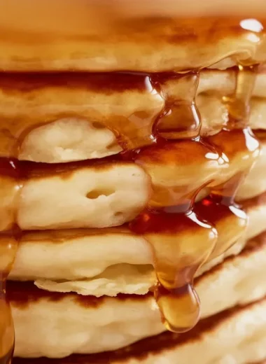 Stack of fluffy pancakes served with syrup and berries on a plate.