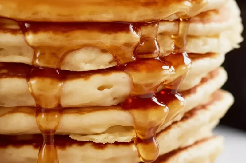 Stack of fluffy pancakes served with syrup and berries on a plate.
