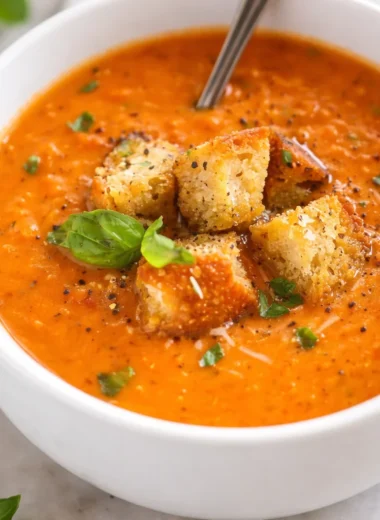 Bowl of creamy Tomato Basil Soup garnished with fresh basil leaves and served hot.