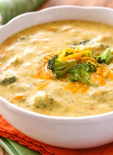 Bowl of creamy broccoli cheddar soup with garnishes on a wooden table.