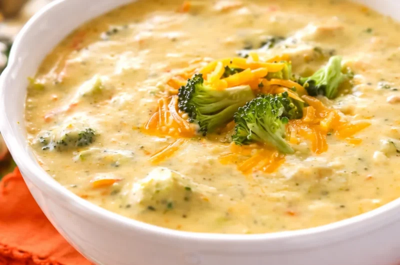 Bowl of creamy broccoli cheddar soup with garnishes on a wooden table.