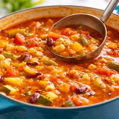 A bowl of cozy minestrone soup filled with veggies and beans, served with bread.